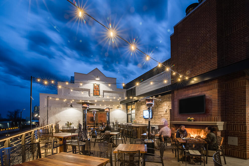 The Rooftop patio and bar at Ginger and Baker with sparkling lights and an outdoor fireplace with big screen tv