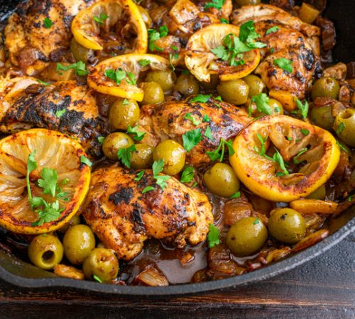 Chicken thighs, olives, and lemons cooked in a cast iron skillet