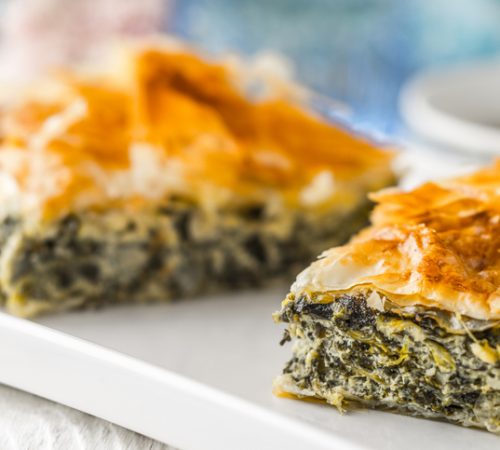 Greek pie spanakopita on the white plate on the white wooden table with  blurred accessorizes horizontal