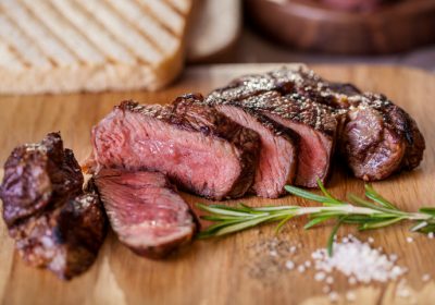 Grilled pork steak pieces with a sprig of rosemary, pepper and salt, fried pieces of bread on a wooden board. Horizontal orientation